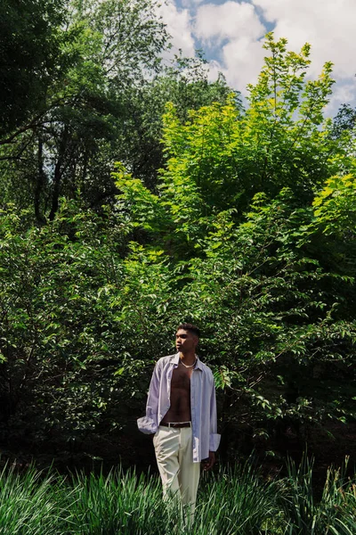 Молодий афроамериканський чоловік в літньому одязі стоїть з рукою в кишені в літньому парку — стокове фото