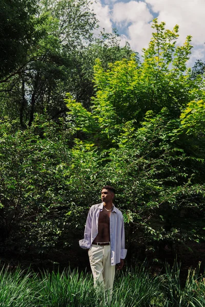 Young african american man in summer clothes standing with hand in pocket in summer park — Stock Photo