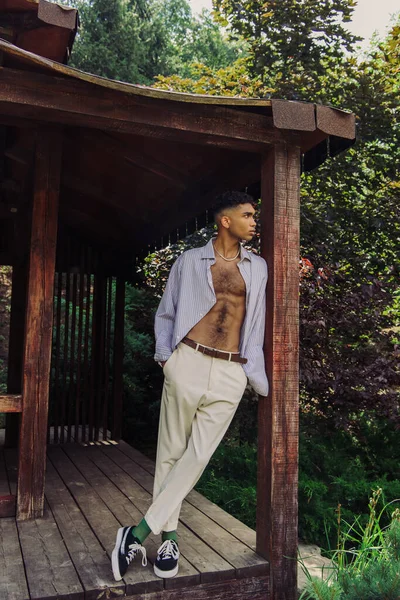 Full length of african american man in white trousers and blue shirt looking away in wooden patio — Fotografia de Stock