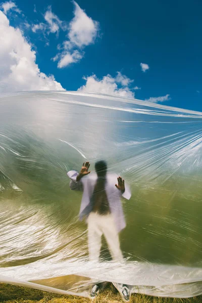 Blurred african american man standing behind cellophane under blue sky with white clouds — Fotografia de Stock