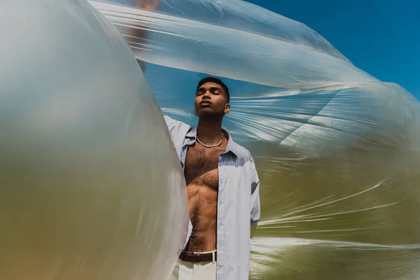 Молодий і модний афроамериканський чоловік із закритими очима біля поліетиленової плівки на відкритому повітрі — стокове фото