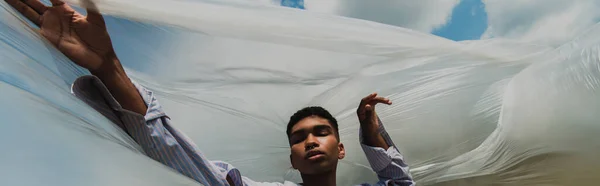 Young african american man with closed eyes under cellophane film outdoors, banner — стоковое фото