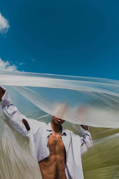 Young african american man in shirt obscuring face with cellophane outdoors - foto de stock