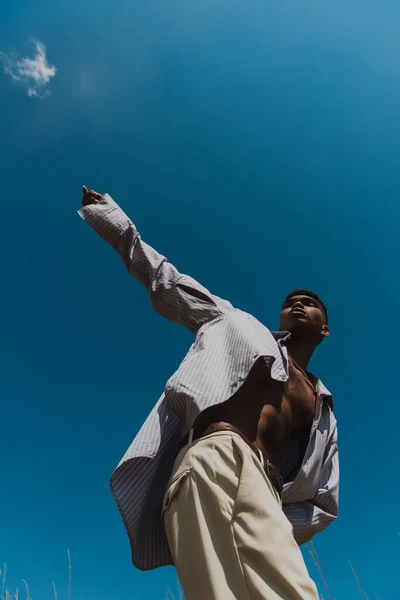 Low angle view of trendy african american man with outstretched hand against clear sky — Stockfoto