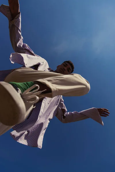 Bottom view of african american man in trendy clothes under blue and clear sky - foto de stock