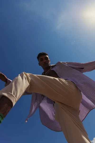 Bottom view of african american man posing in trendy summer clothes under blue sunny sky - foto de stock