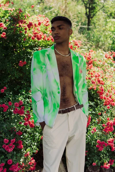 African american man in trendy blazer standing with hands in pockets of white trousers in park — стоковое фото