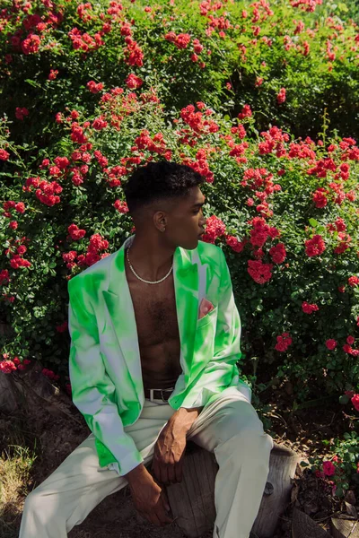 African american man in fashionable blazer looking at blossoming bushes in park — Stock Photo