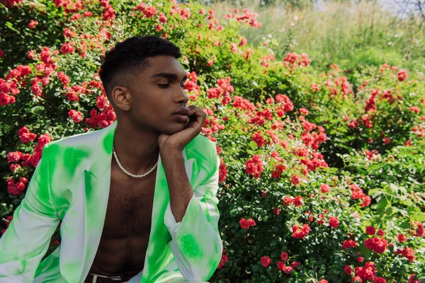 African american man in fashionable blazer sitting with hand near face in park — стоковое фото