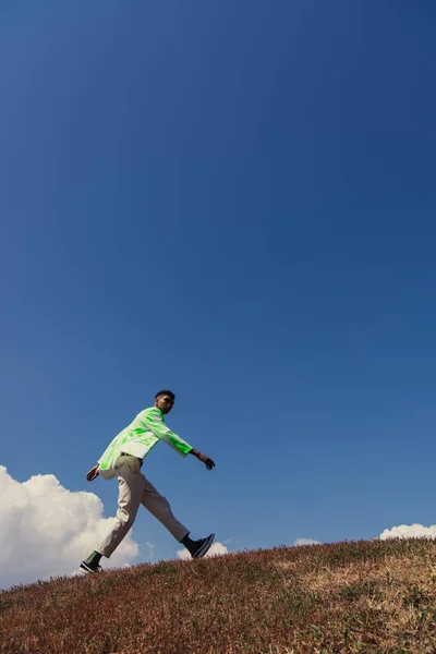 Side view of african american man in trendy summer outfit walking in field — Photo de stock