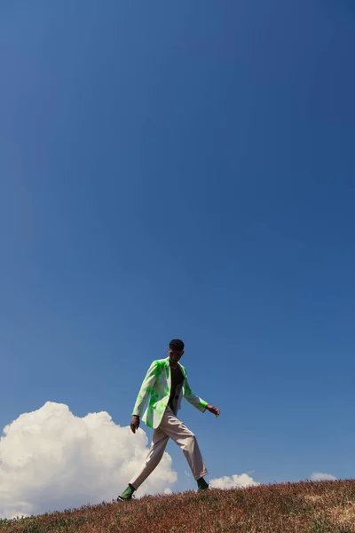 Молодий афроамериканський чоловік у стильному літньому вбранні, що йде полем під блакитним небом — стокове фото