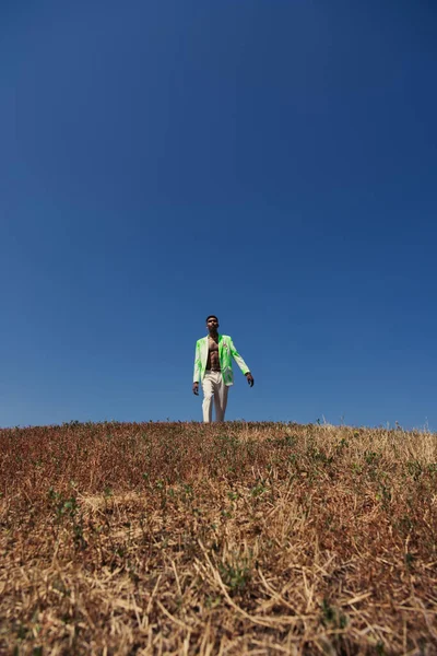 Trendy african american man walking in meadow under blue and clear sky — Fotografia de Stock