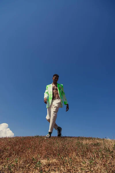 Full length of fashionable african american man walking in field against blue sky — Stock Photo