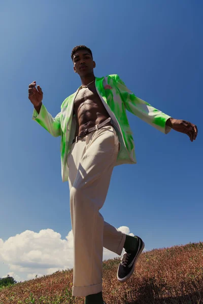 Низький кут зору афроамериканця в білих штанях і блістері проти блакитного неба — стокове фото