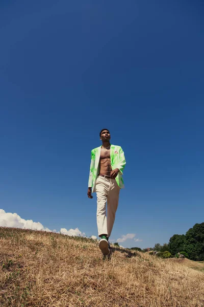 Повна довжина модного афроамериканця в літньому вбранні, що йде під блакитним небом на лузі — стокове фото
