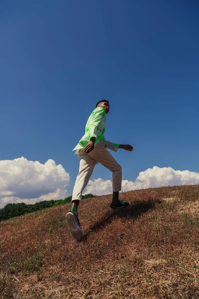Back view of young african american man in summer clothes running in green field — Photo de stock