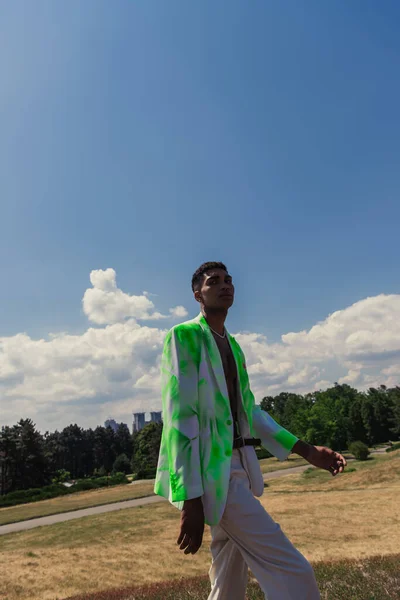 Молодий афроамериканський чоловік в зеленому і білому блістері, що йде в полі поблизу парку — стокове фото