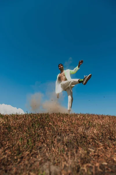 Young and trendy african american man posing on one leg in grassy field under clear sky — Photo de stock