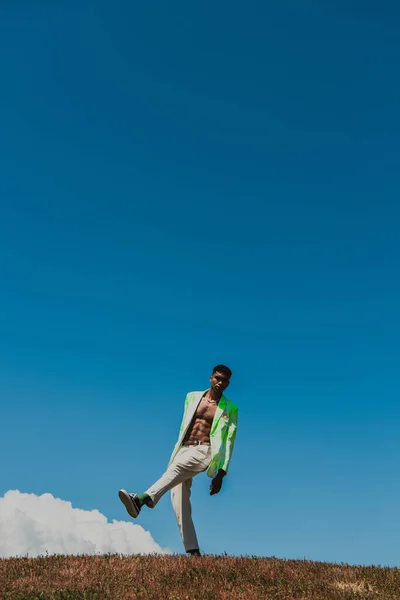 Full length of african american man in white trousers and blazer under blue sky in field — Stock Photo