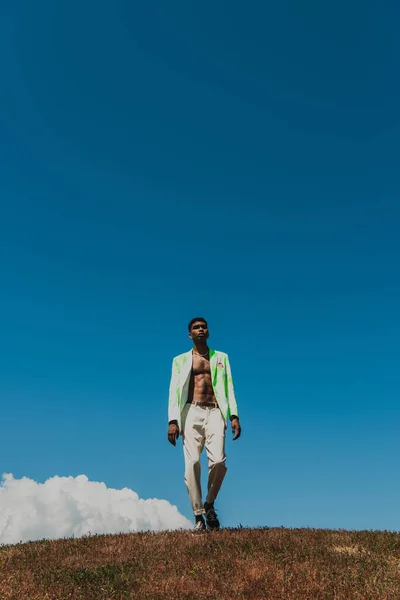 Full length of stylish african american man in summer outfit walking in meadow under clear sky — Stock Photo