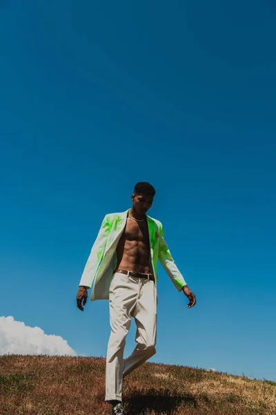 African american man in white and green blazer walking in field on summer day — Photo de stock