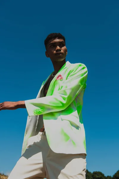 Low angle view of african american man in white and green blazer looking away under blue sky — стоковое фото