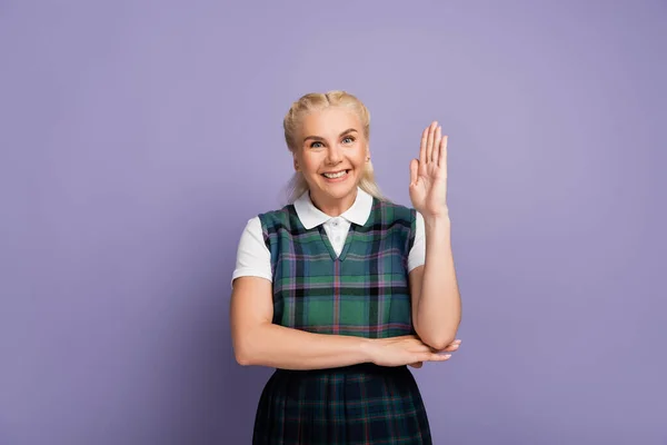 Smiling blonde student rising hand isolated on purple — Stock Photo