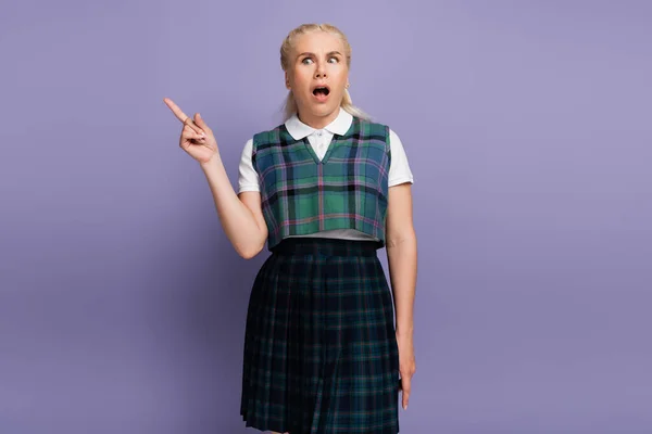 Shocked blonde student pointing with finger on purple background — Photo de stock