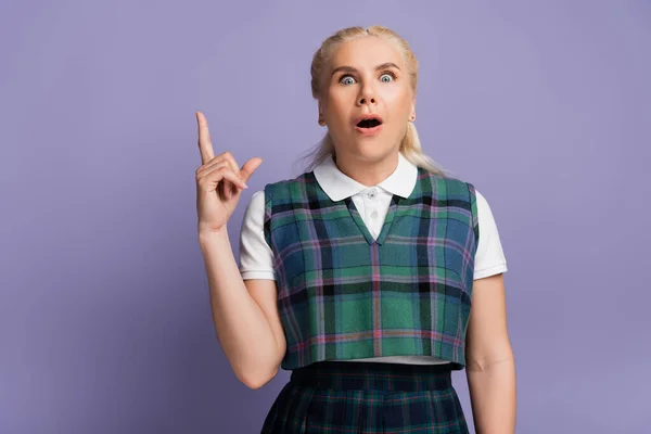 Shocked blonde student in uniform pointing with finger isolated on purple — Foto stock