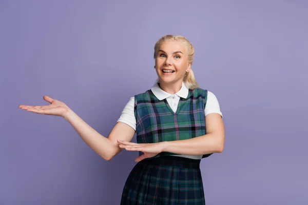 Cheerful student in uniform pointing with hand isolated on purple — Stock Photo