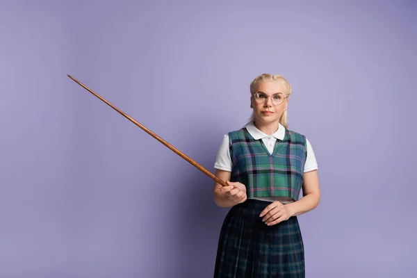 Blonde student in eyeglasses holding pointer on purple background — стоковое фото