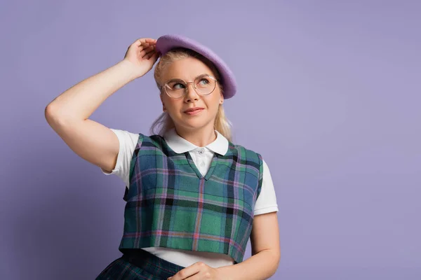 Blonde student in eyeglasses holding beret isolated on purple — стоковое фото