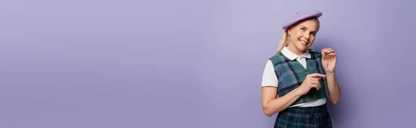 Happy blonde student in beret holding eyeglasses on purple background, banner — Stockfoto