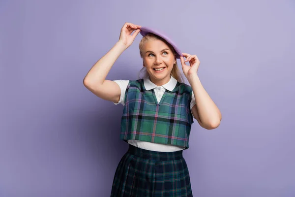 Smiling student in plaid uniform wearing beret on purple background — Stockfoto