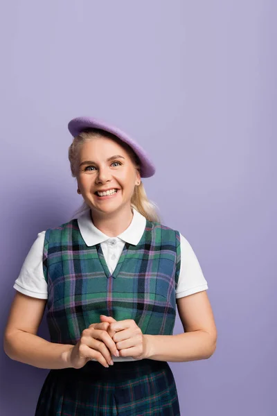 Positive student in plaid uniform and beret looking at camera on purple background — Fotografia de Stock