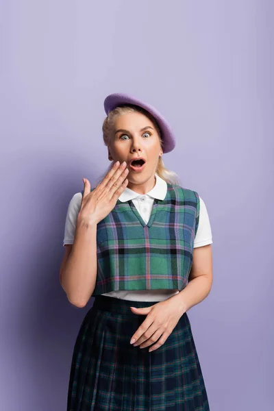 Shocked student in beret looking at camera on purple background — Photo de stock