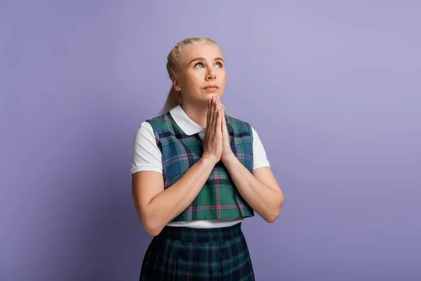 Student in checkered uniform doing praying hands isolated on purple - foto de stock