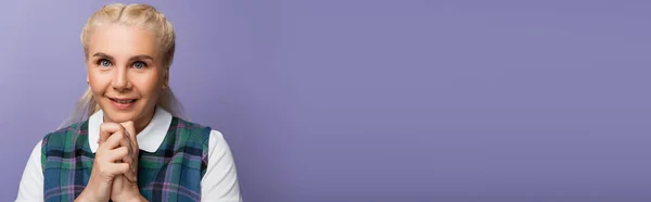 Blonde student with clenched hands smiling at camera isolated on purple, banner — Photo de stock