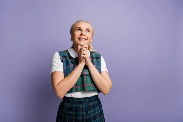 Dreamy student with clenched hands looking up isolated on purple — стоковое фото