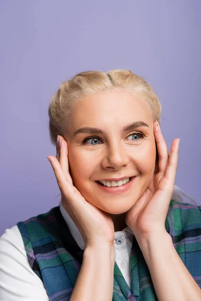 Portrait of smiling blonde student touching face isolated on purple — Fotografia de Stock