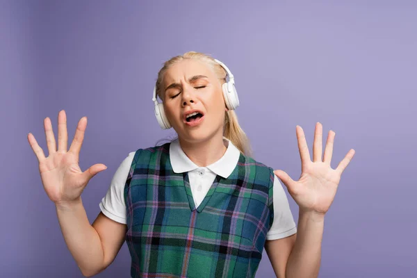 Blonde student in headphones singing isolated on purple — стоковое фото