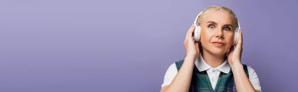 Student in shirt and vest listening music in headphones isolated on purple, banner — стоковое фото