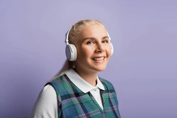 Портрет веселого студента в навушниках, який дивиться на камеру ізольовано на фіолетовому — стокове фото