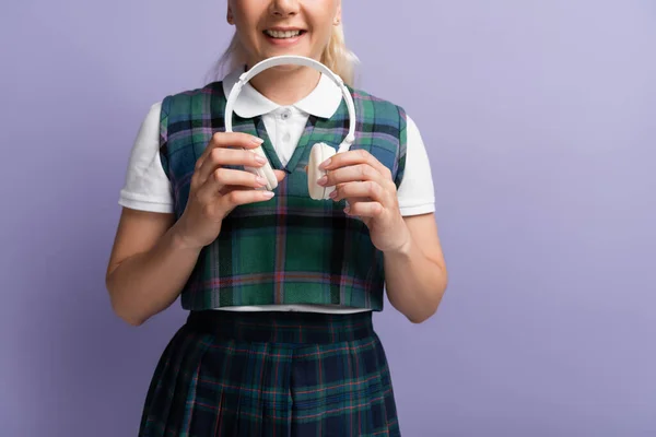 Cropped view of smiling student holding wireless headphones isolated on purple — Stockfoto