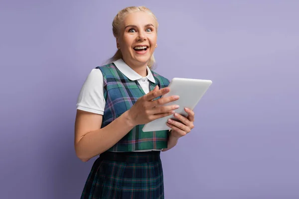 Excited student in vest holding digital tablet isolated on purple — стоковое фото