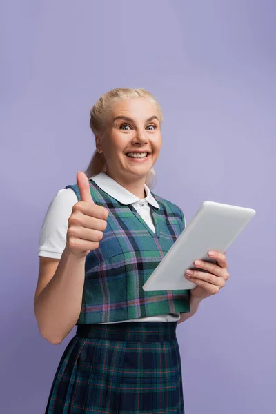 Positive student showing thumb up and holding digital tablet isolated on purple — Stock Photo