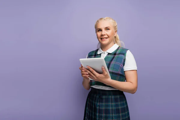 Smiling student in plaid vest holding digital tablet and looking at camera isolated on purple — Stockfoto