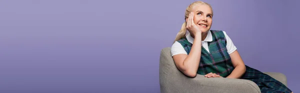 Student in uniform smiling while sitting on armchair isolated on purple, banner — Stock Photo