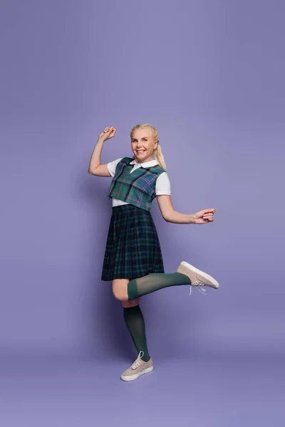 Full length of smiling student in uniform standing on purple background — стоковое фото