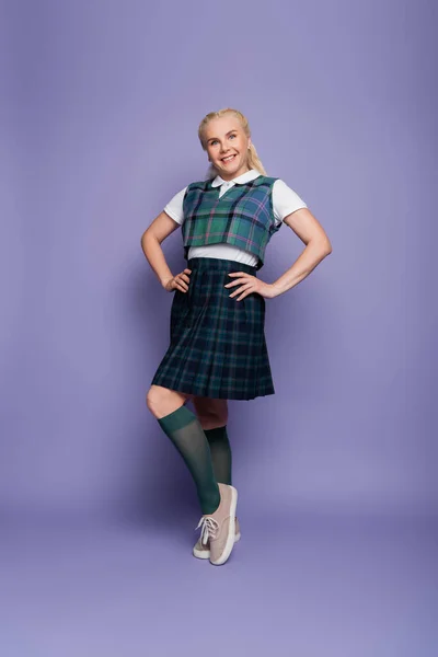 Full length of smiling student in plaid skirt standing on purple background — Foto stock